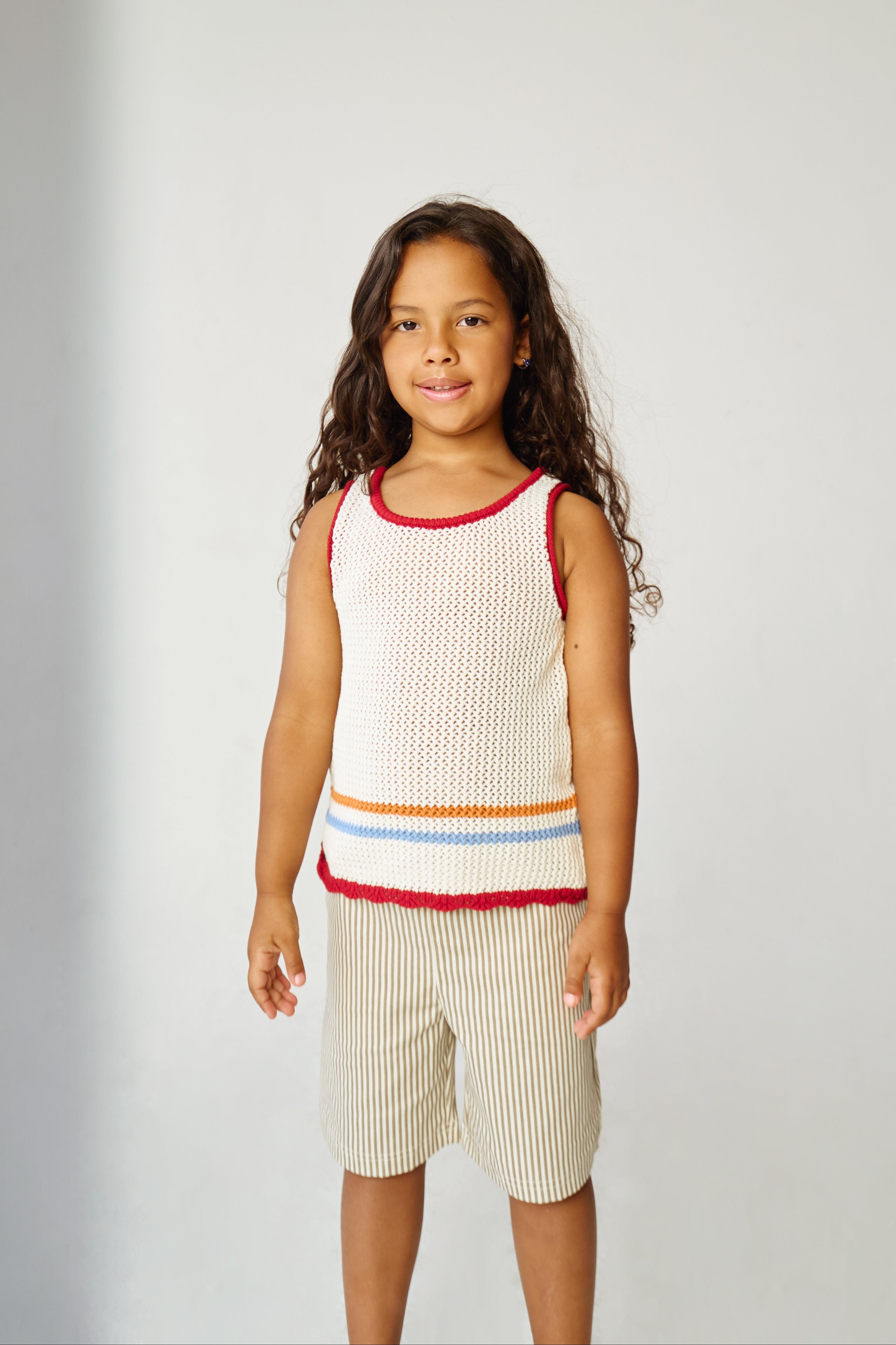 Kid wearing white open knit tank top with khaki striped shorts.