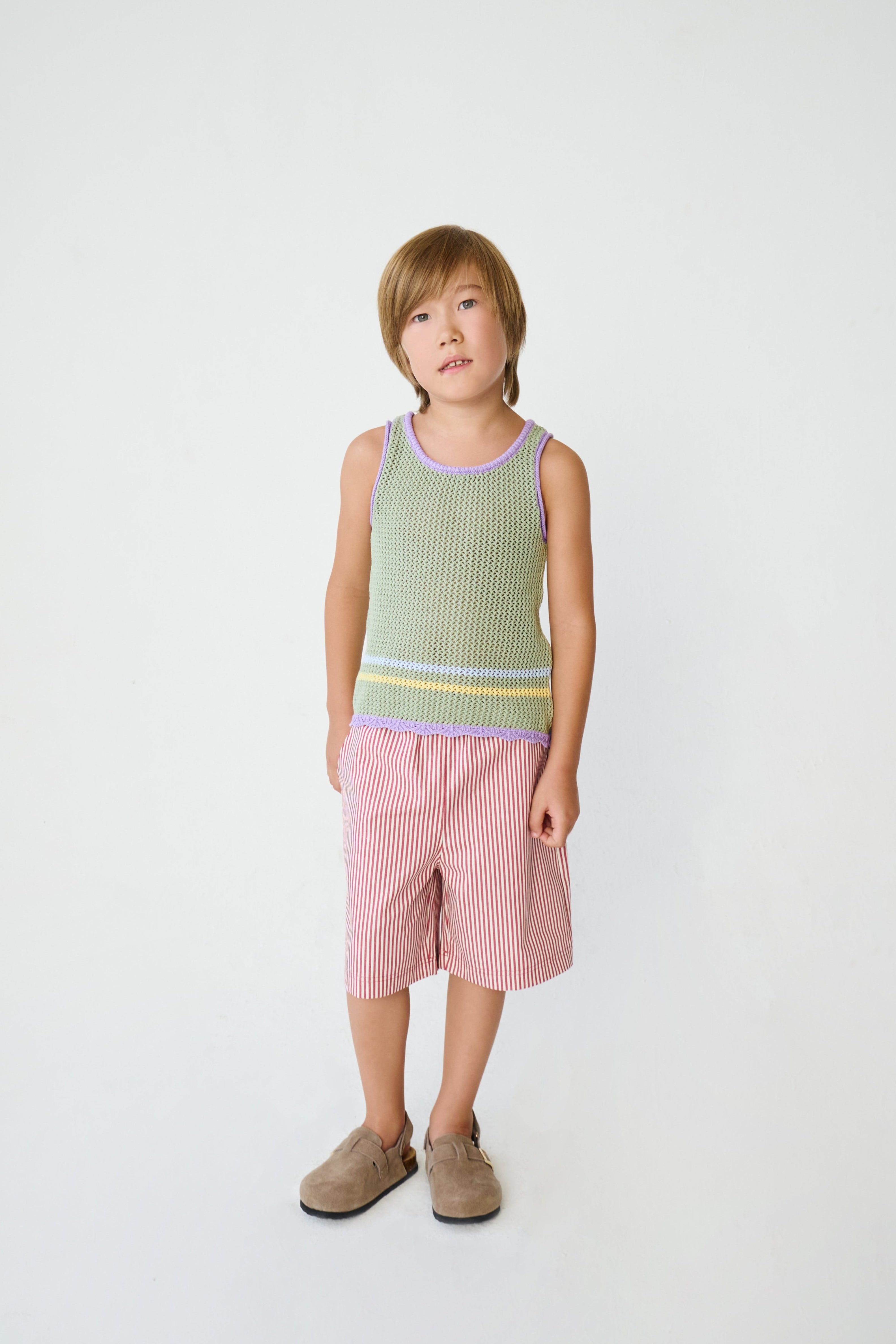 Kid wearing green open knit tank top with red stripe shorts.